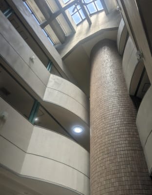 会社エントランスの吹き抜け。高い天井まで伸びる円柱状の構造物と曲線的な壁面デザイン。上部に大きな窓があり自然光が差し込んでいる。